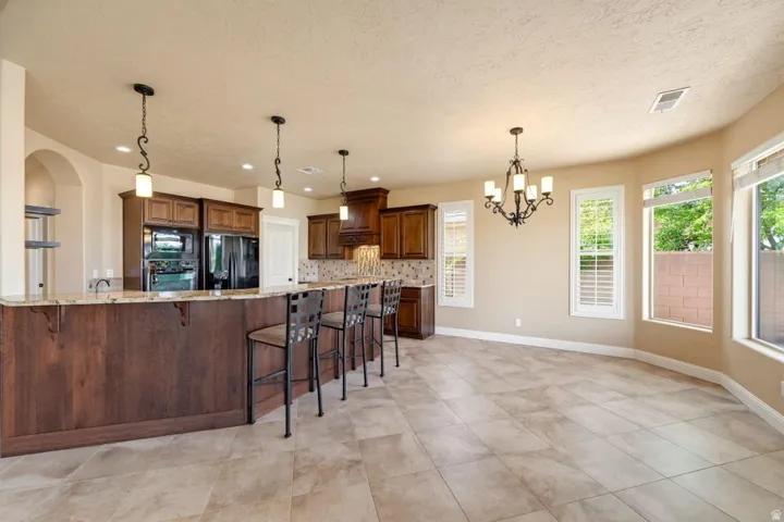 Kitchen featuring a kitchen bar, light stone counters, suspended lighting, decorative backsplash, and black appliances