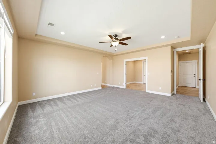 Unfurnished bedroom featuring arched walkways, a ceiling fan, recessed lighting, a raised ceiling, and light colored carpet