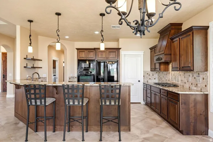 Kitchen with light stone counters, a breakfast bar, arched walkways, black appliances, and decorative light fixtures