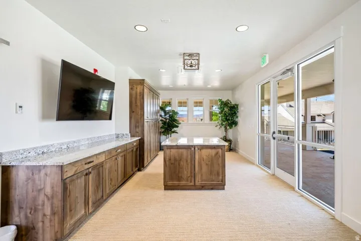 Kitchen featuring light carpet, recessed lighting, light stone countertops, wood finish cabinetry, and a center island