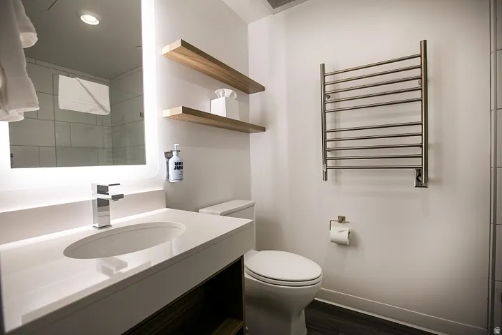 Bathroom featuring a towel warmer, radiator heating unit, vanity, dark wood-type flooring, and recessed lighting