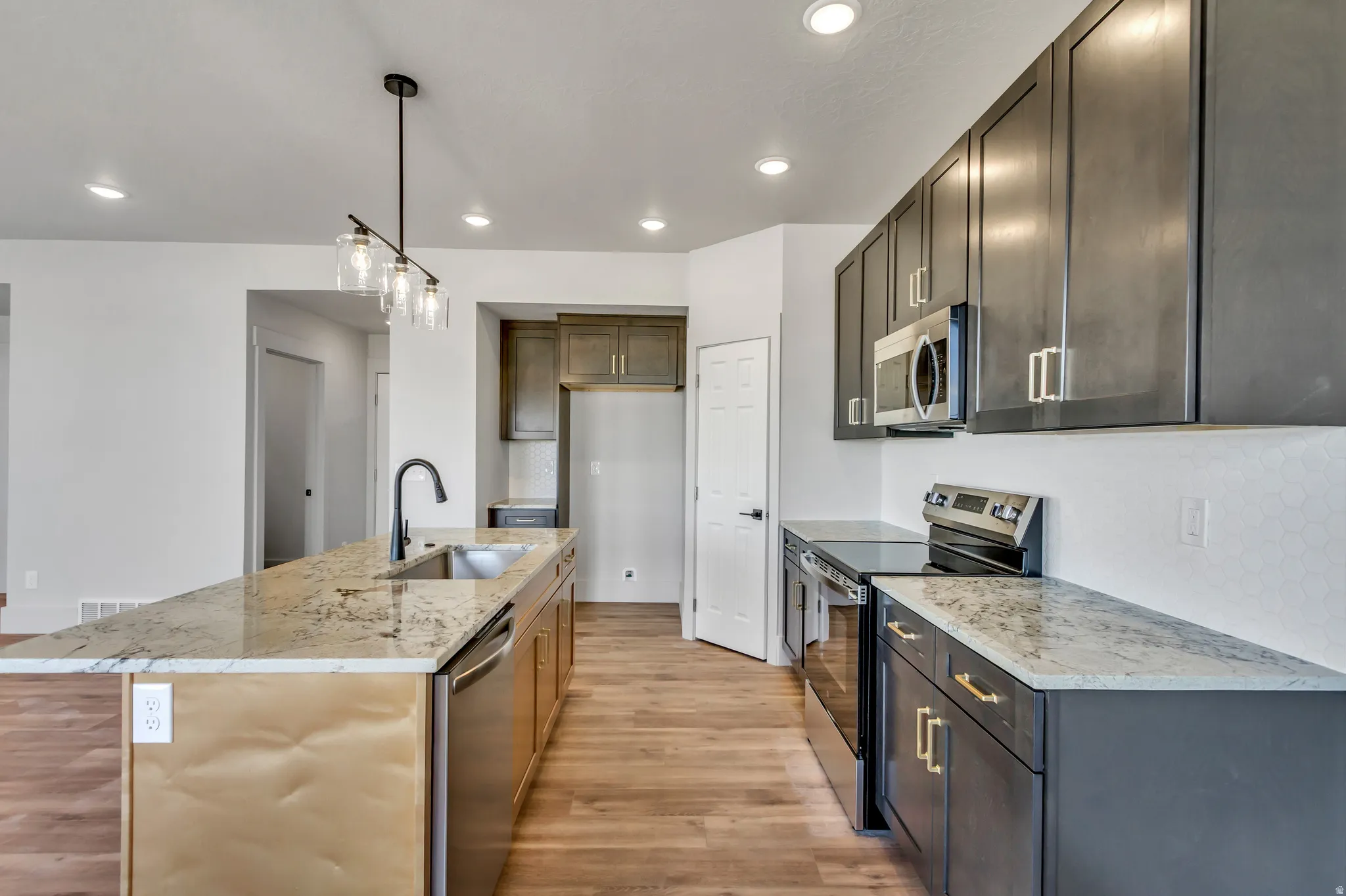 Kitchen with stainless steel appliances, light wood-type flooring, light stone countertops, an island with sink, and decorative backsplash
