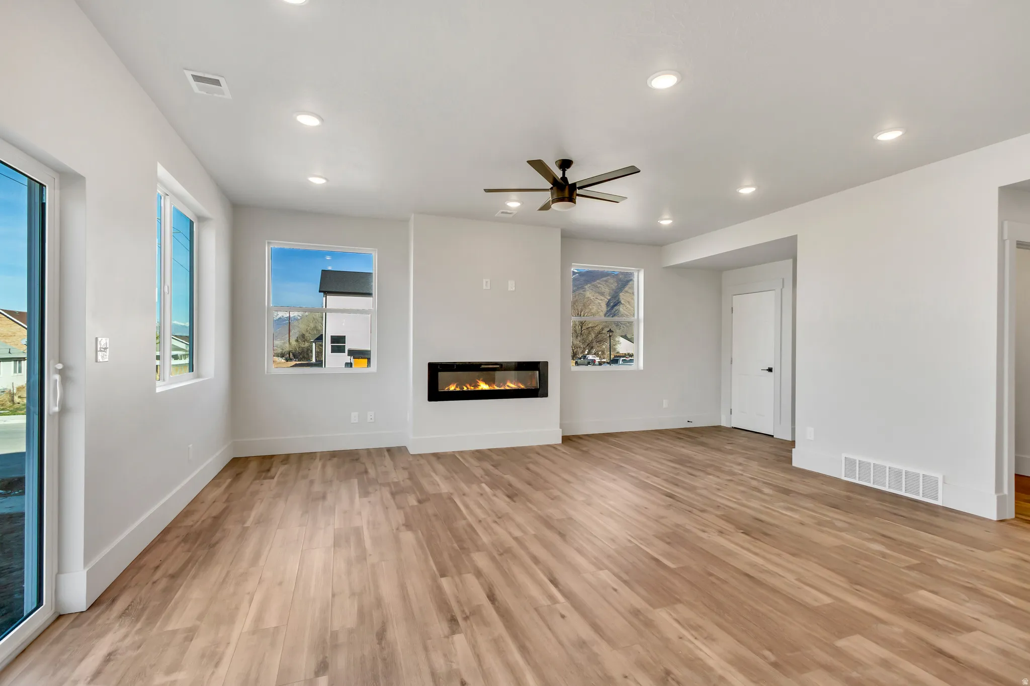 Unfurnished living room featuring ceiling fan, a glass covered fireplace, light wood-type flooring, and recessed lighting