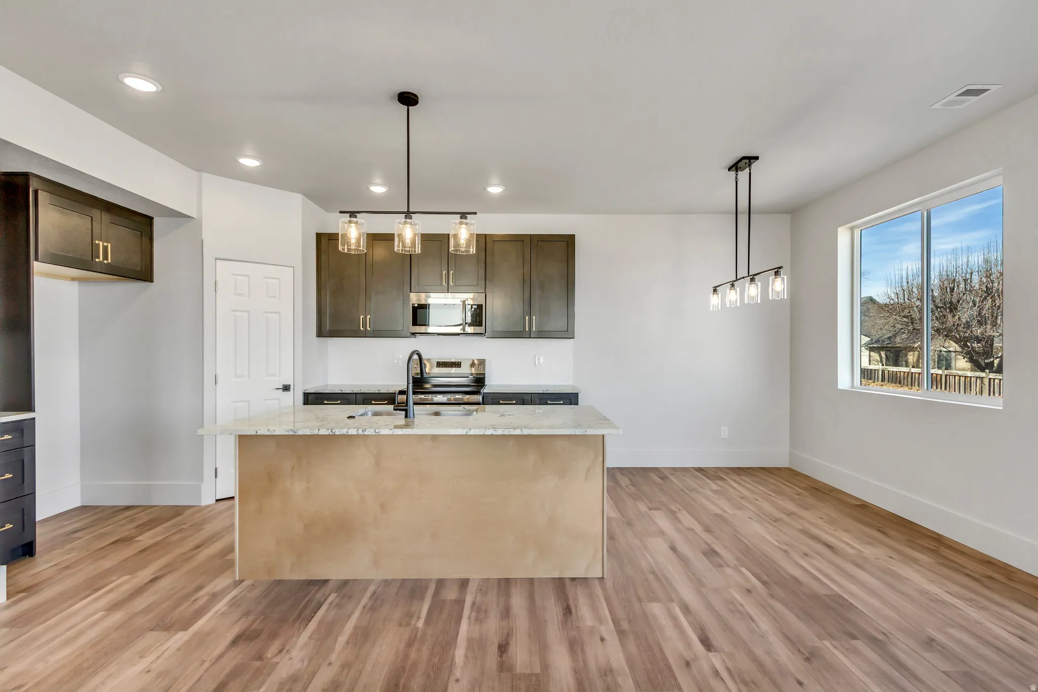 Kitchen featuring light stone counters, decorative light fixtures, dark wood finish cabinetry, and stainless steel appliances