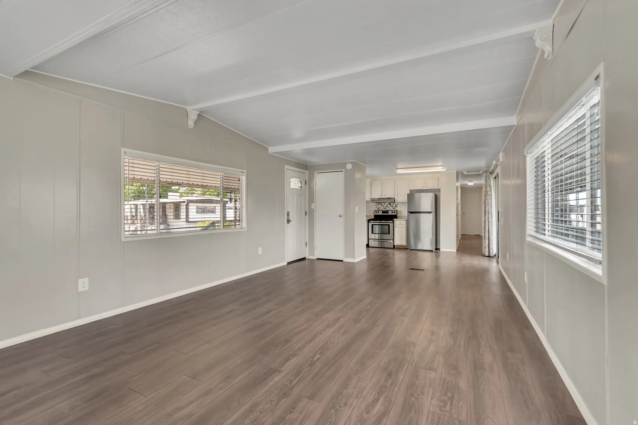 Unfurnished living room with dark wood-style flooring, lofted ceiling with beams, and a decorative wall