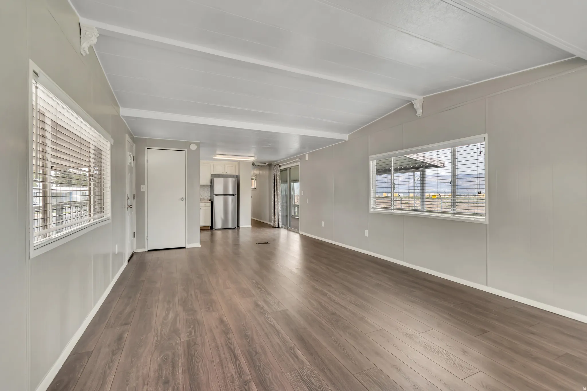 Unfurnished living room featuring dark wood-style floors and vaulted ceiling with beams