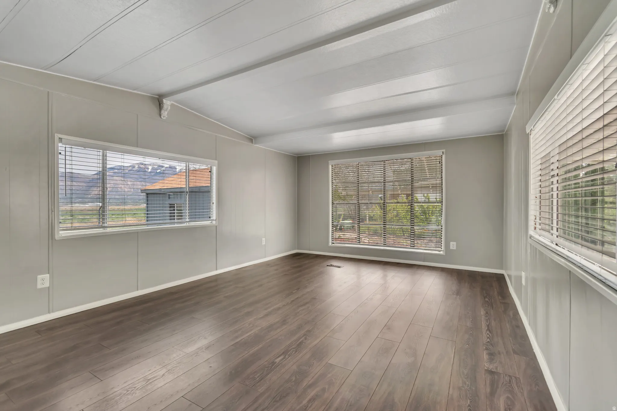 Unfurnished room with dark wood-style floors and vaulted ceiling with beams