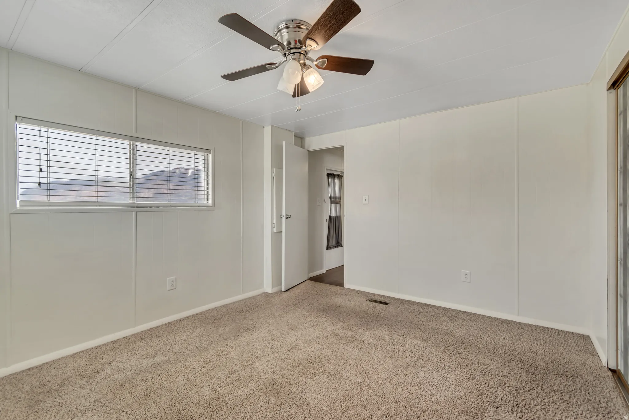 Carpeted empty room featuring a decorative wall and a ceiling fan