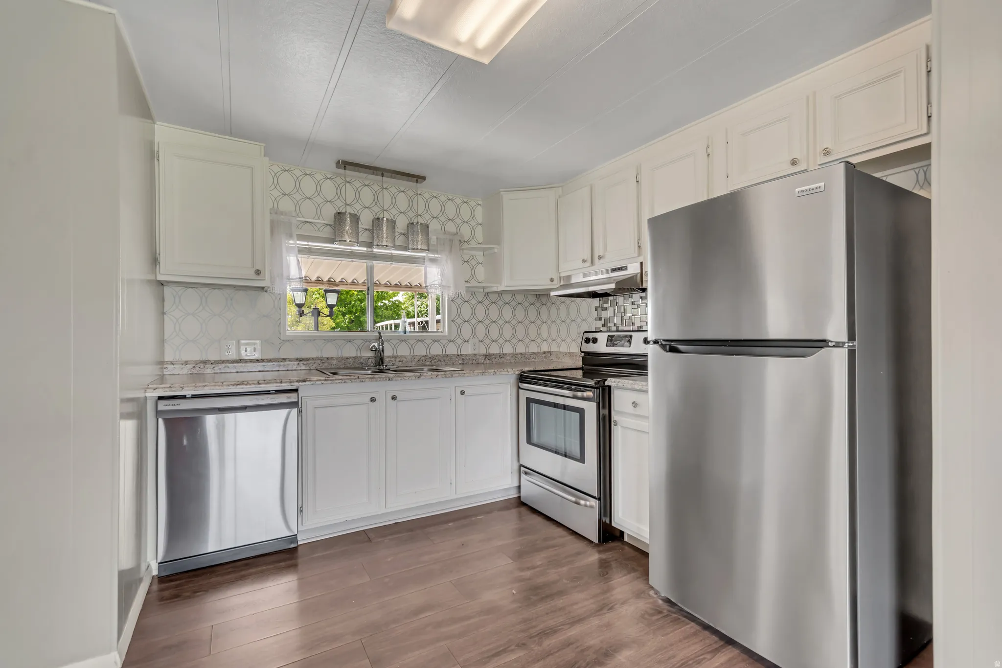 Kitchen with stainless steel appliances, light stone counters, dark wood-style floors, and white cabinetry