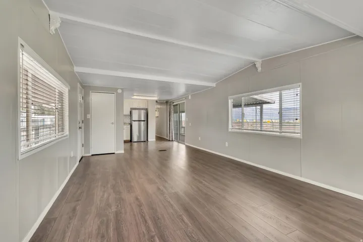 Unfurnished living room featuring dark wood-style floors and vaulted ceiling with beams
