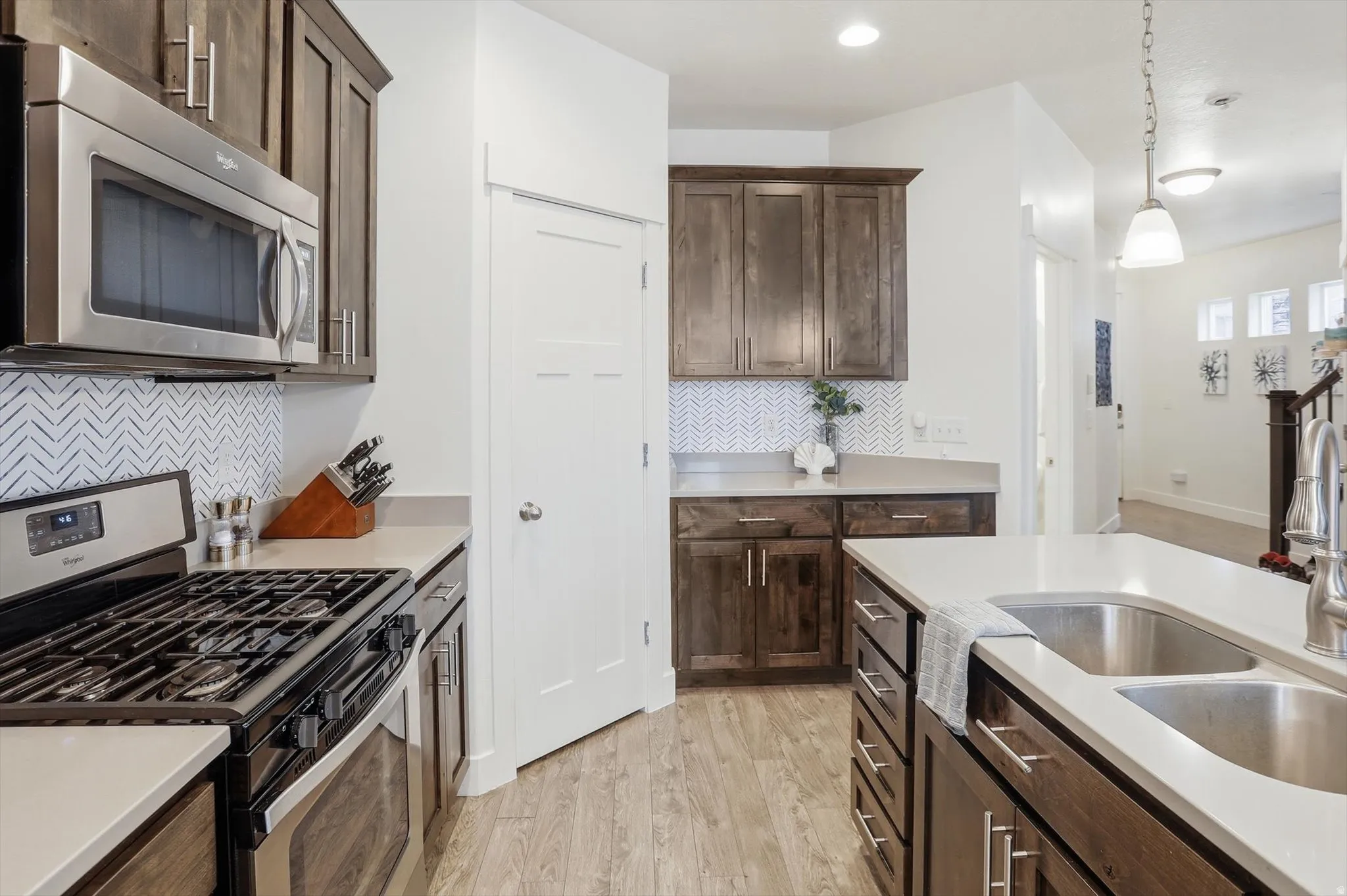 Kitchen featuring dark wood finish cabinets, stainless steel appliances, backsplash, light wood finished floors, and decorative light fixtures