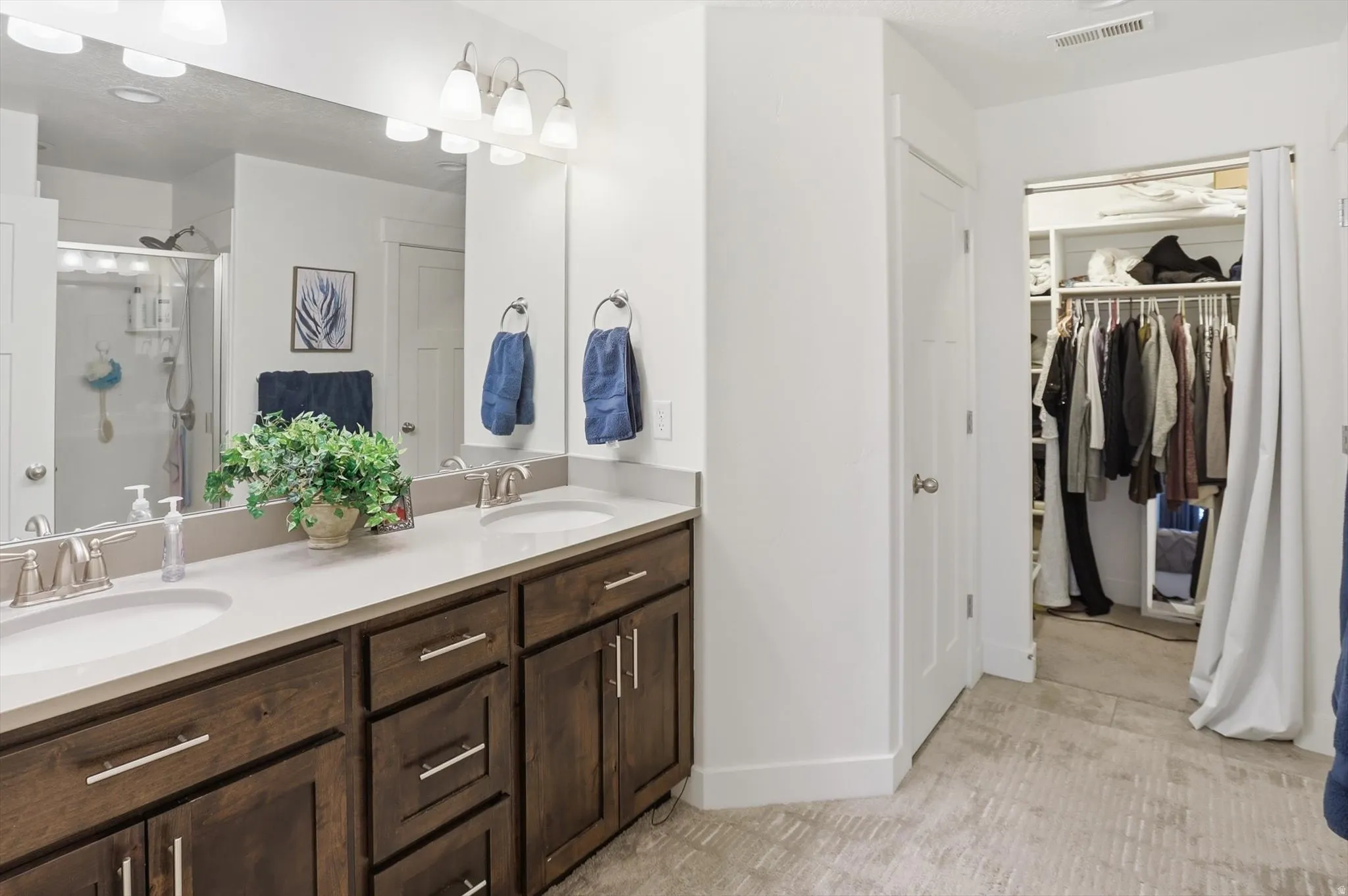 Full bathroom featuring double vanity, a spacious closet, a stall shower, and light colored carpet