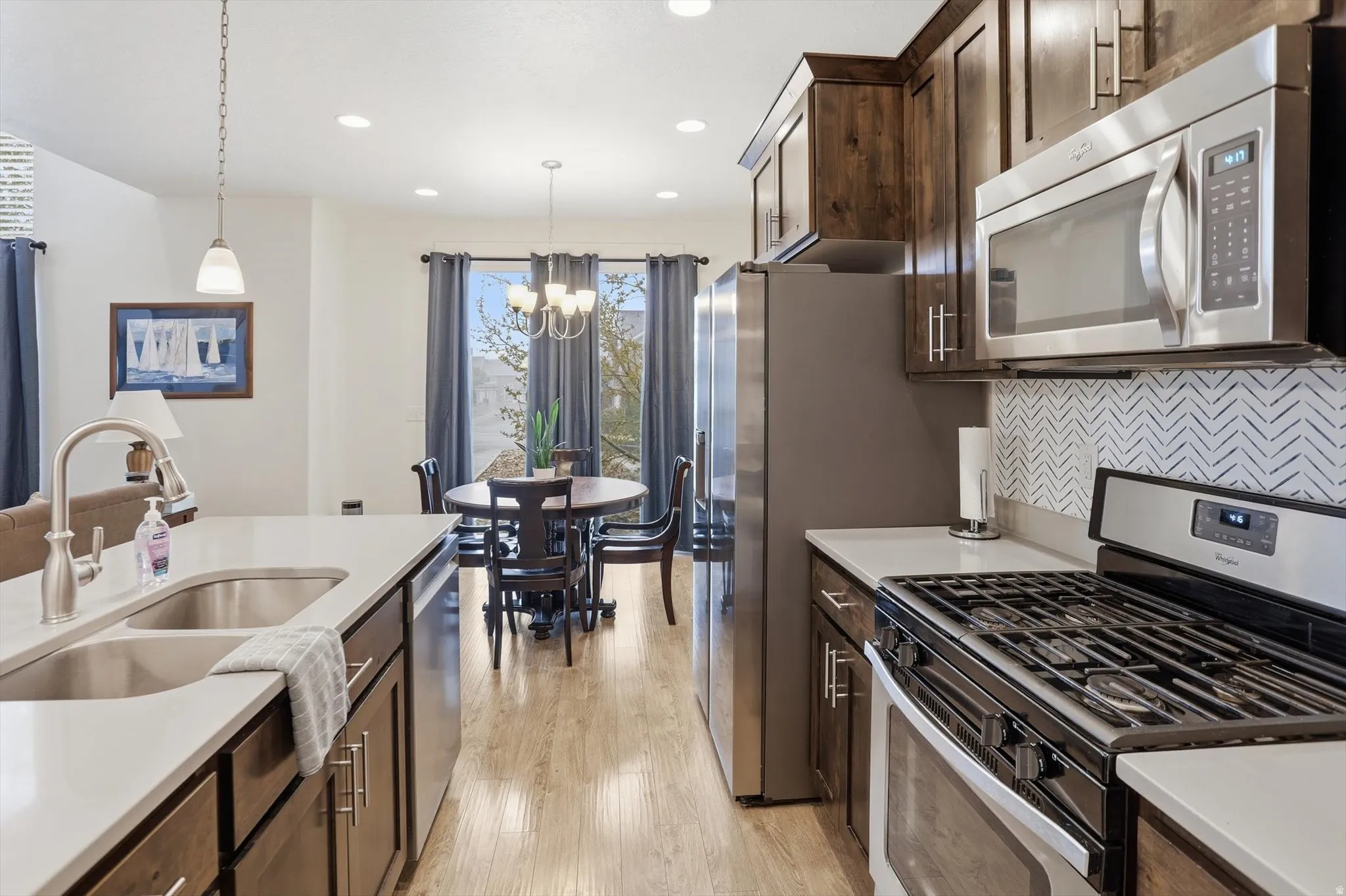 Kitchen featuring stainless steel appliances, dark wood finish cabinets, light wood finished floors, backsplash, and light stone counters