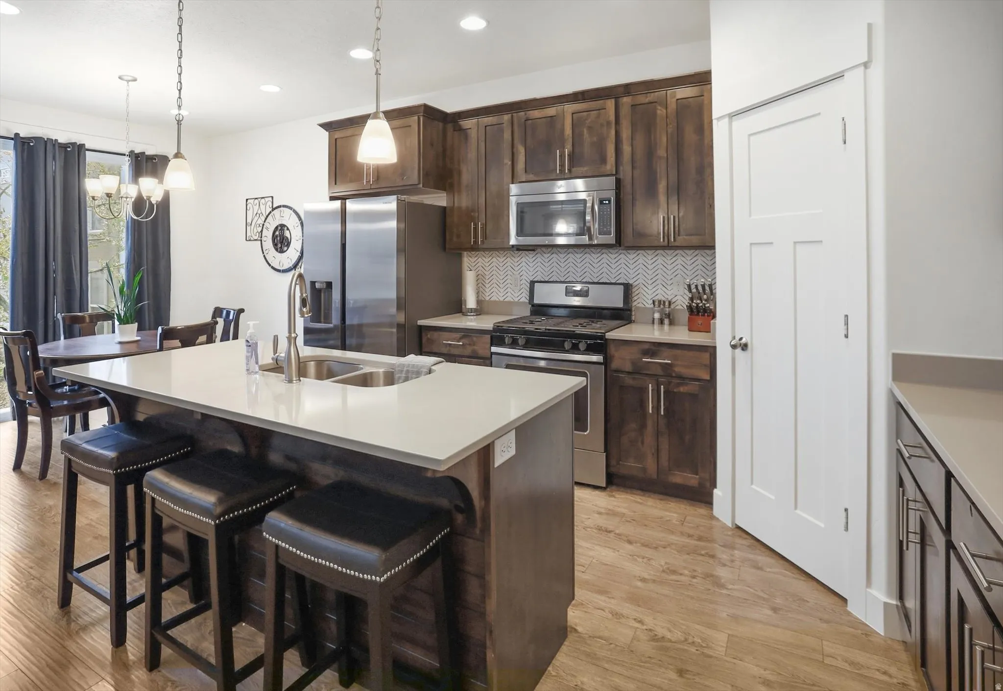 Kitchen featuring stainless steel appliances, a kitchen bar, an island with sink, decorative backsplash, and light wood-type flooring