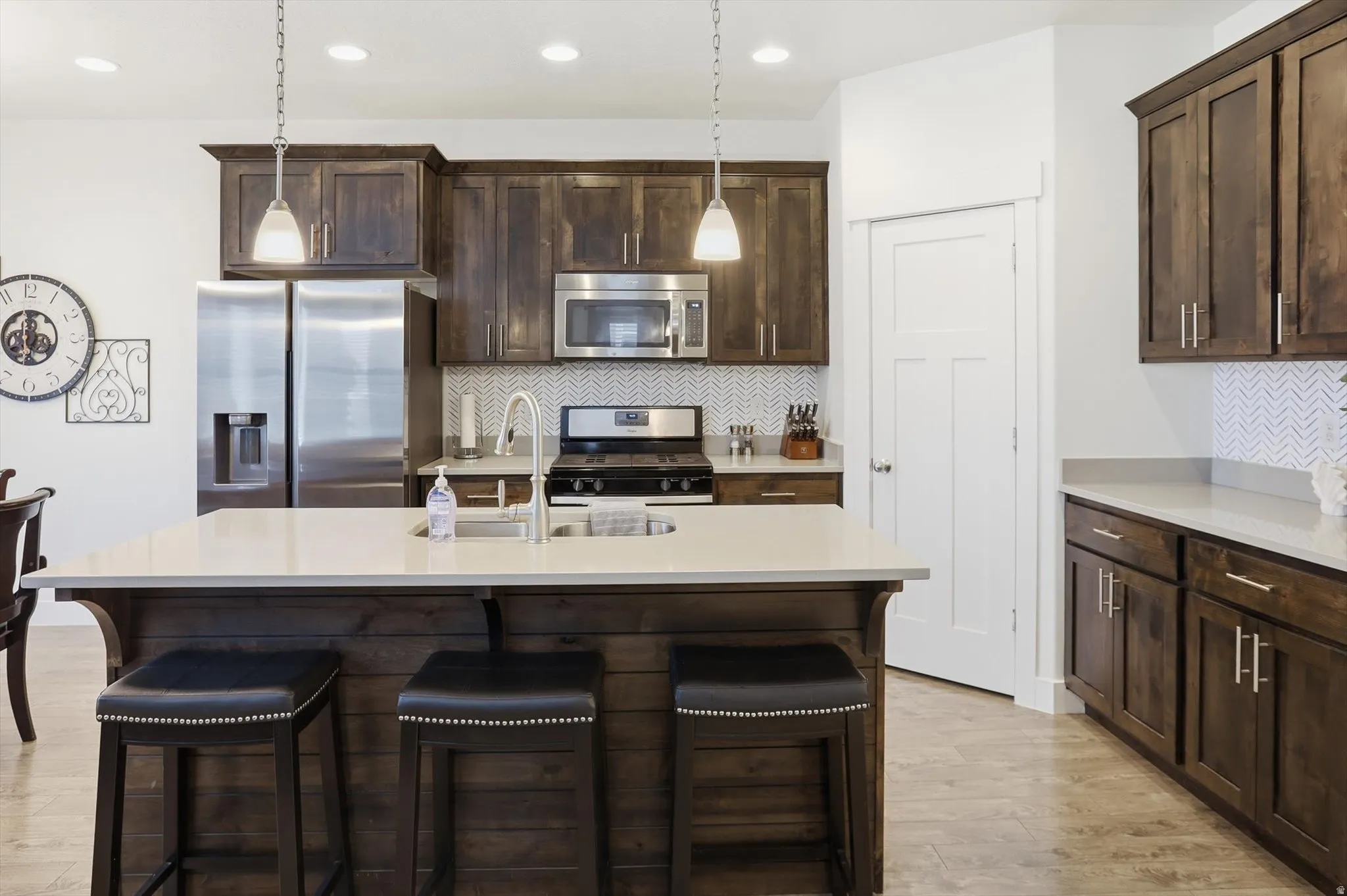 Kitchen with dark wood finish cabinetry, backsplash, stainless steel appliances, and light stone countertops