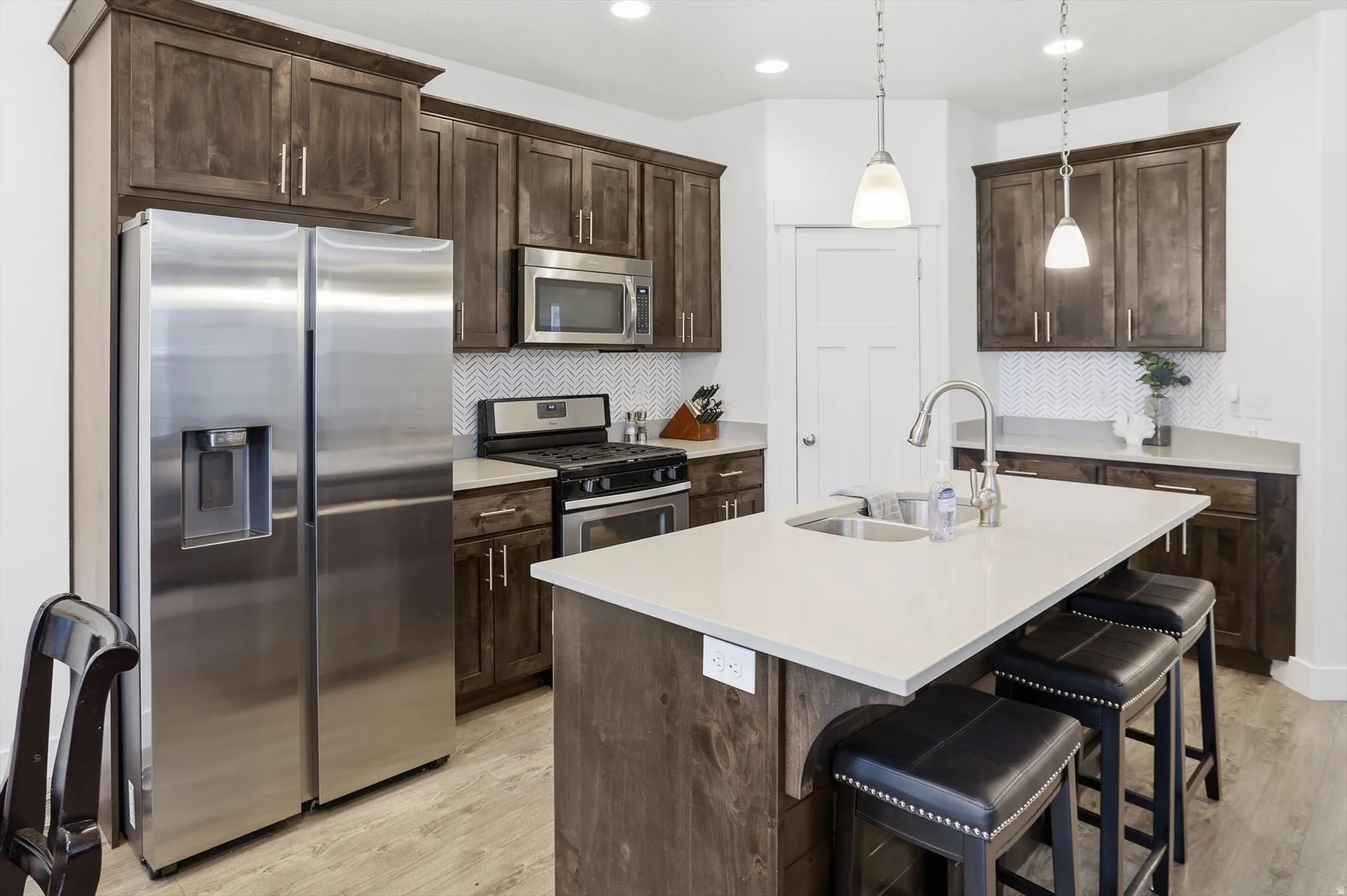 Kitchen featuring stainless steel appliances, dark wood finish cabinets, an island with sink, and a kitchen breakfast bar