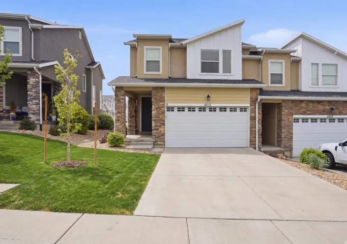 View of front of home with stone siding, driveway, a garage, board and batten siding, and a front yard