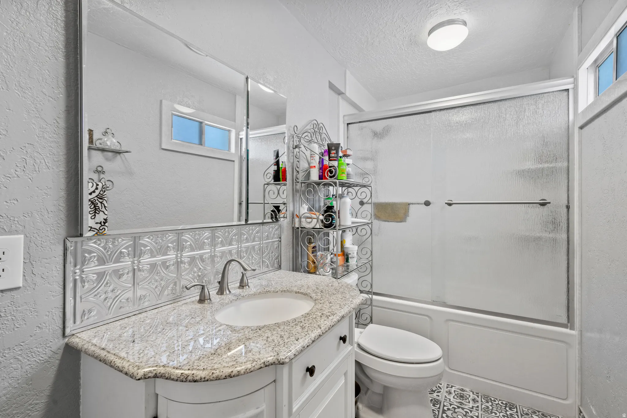 Bathroom with a textured wall, vanity, shower / bath combination with glass door, and a textured ceiling