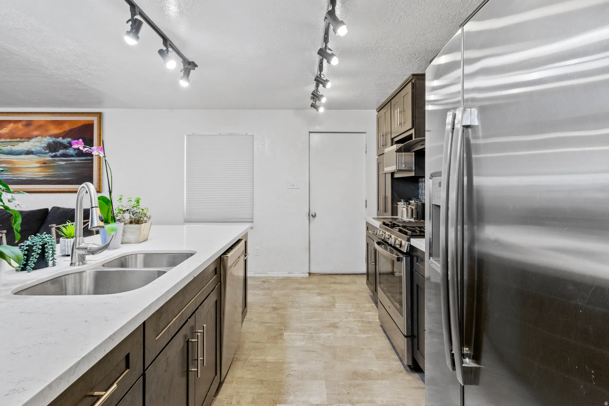 Kitchen featuring stainless steel appliances, light stone countertops, a textured ceiling, and light wood-style flooring