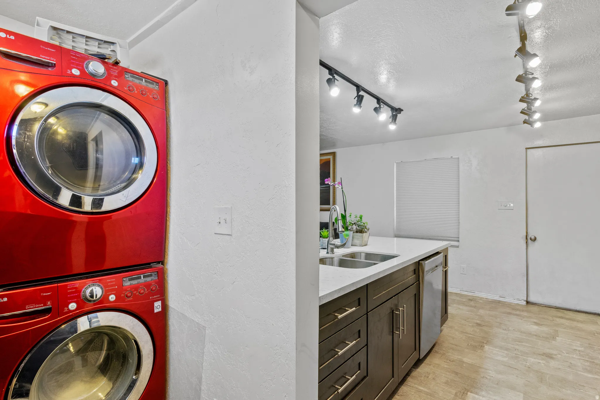 Laundry area with light wood finished floors, a textured wall, stacked washer and dryer, and a textured ceiling