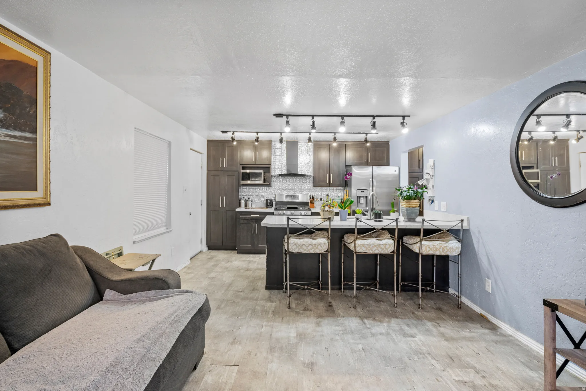 Kitchen with a kitchen breakfast bar, decorative backsplash, a textured ceiling, stainless steel appliances, and dark wood finish cabinets