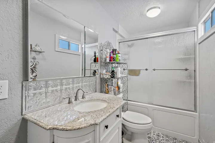 Bathroom with a textured wall, vanity, shower / bath combination with glass door, and a textured ceiling