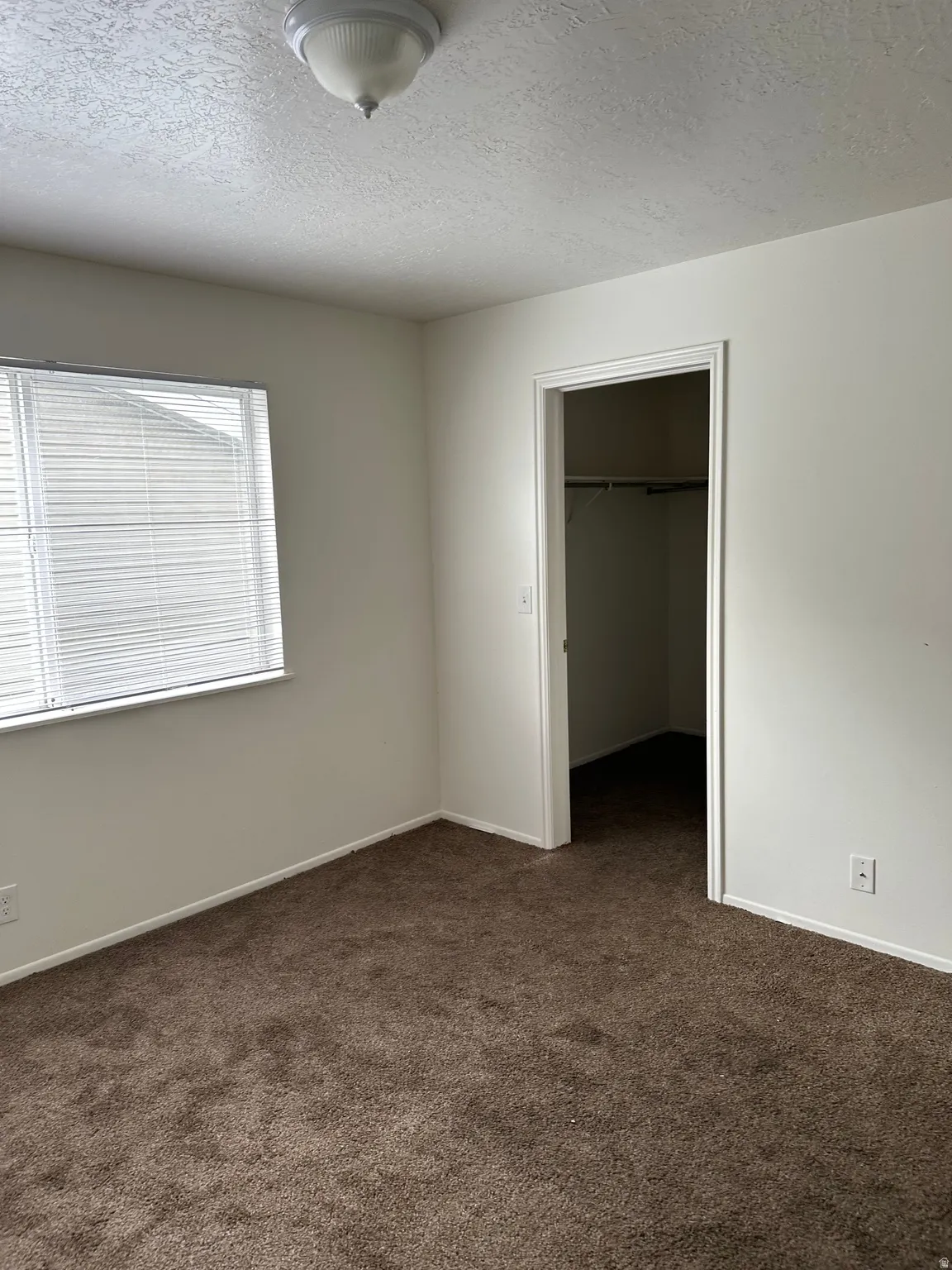 Unfurnished bedroom featuring dark carpet, a textured ceiling, and a walk in closet