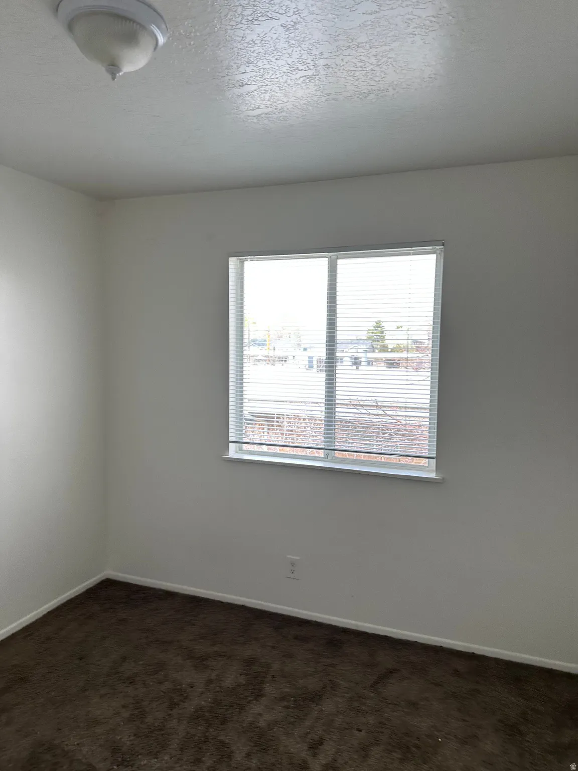 Empty room with dark carpet and a textured ceiling