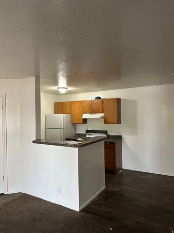 Kitchen featuring wood finish cabinetry, dark countertops, white appliances, a peninsula, and a textured ceiling