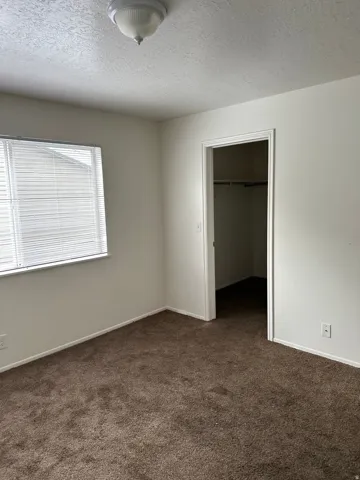Unfurnished bedroom featuring dark carpet, a textured ceiling, and a walk in closet