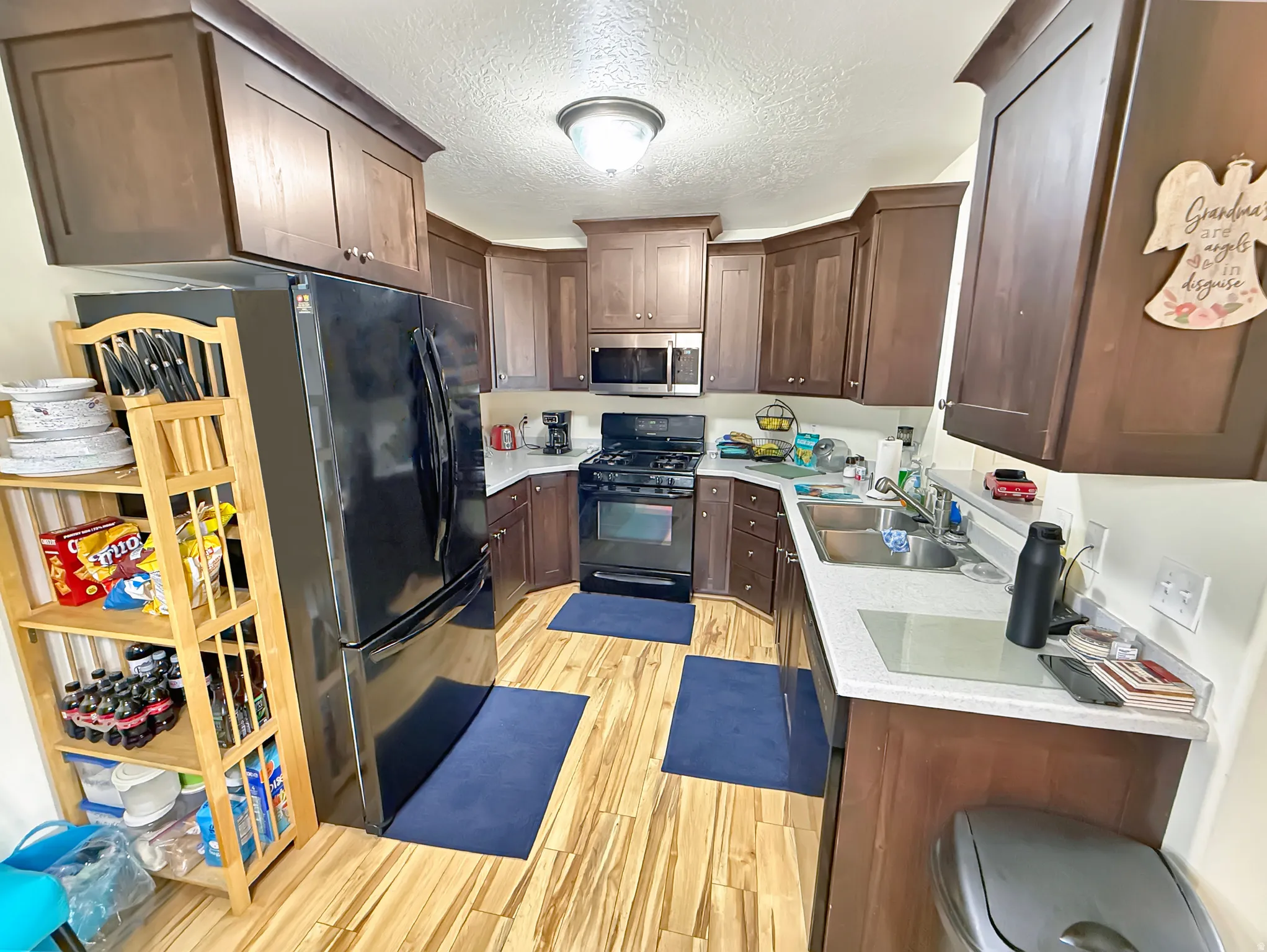 Kitchen featuring black appliances, dark wood finish cabinetry, a textured ceiling, light wood finished floors, and light stone countertops