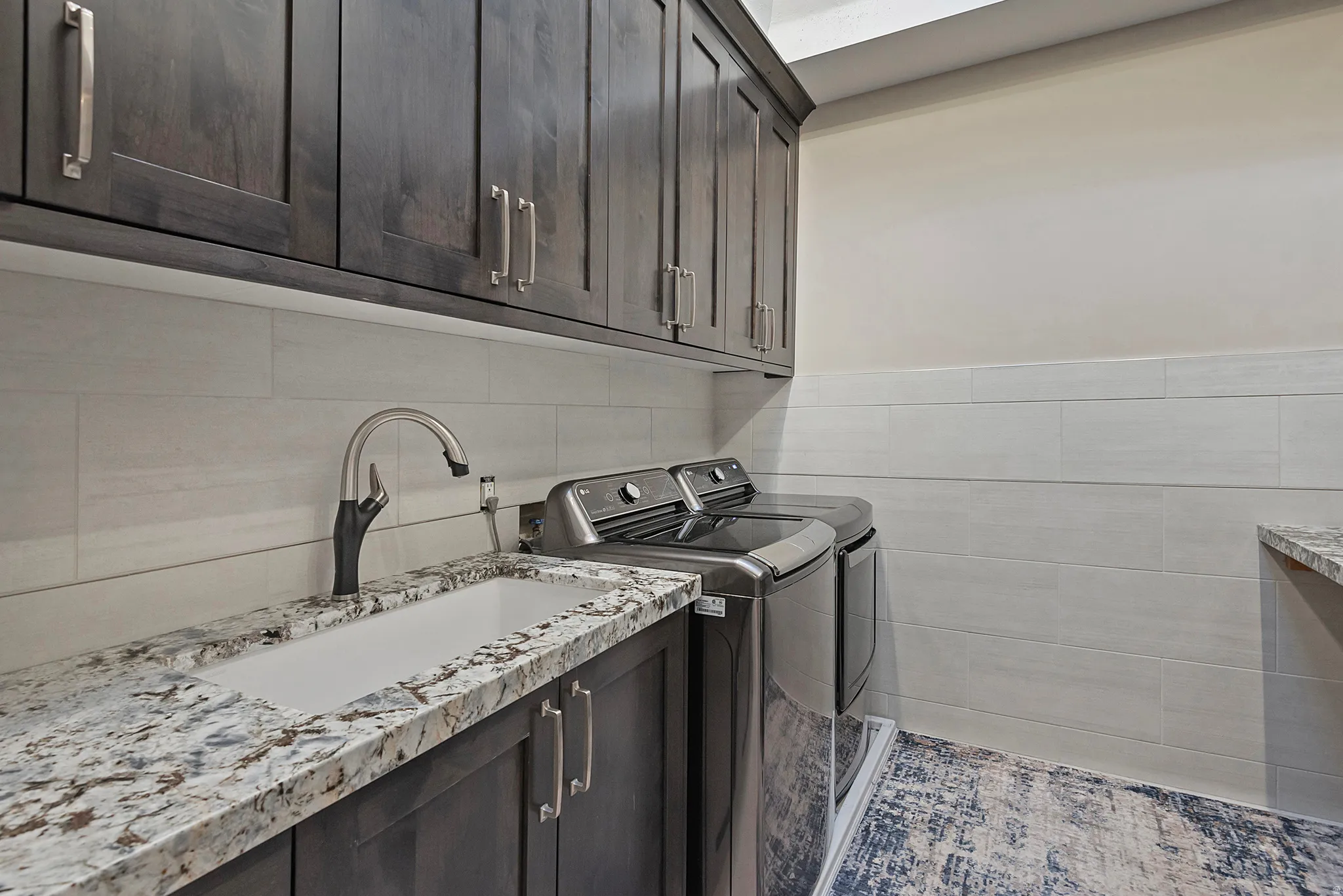 Laundry room with independent washer and dryer, tile walls, and cabinet space