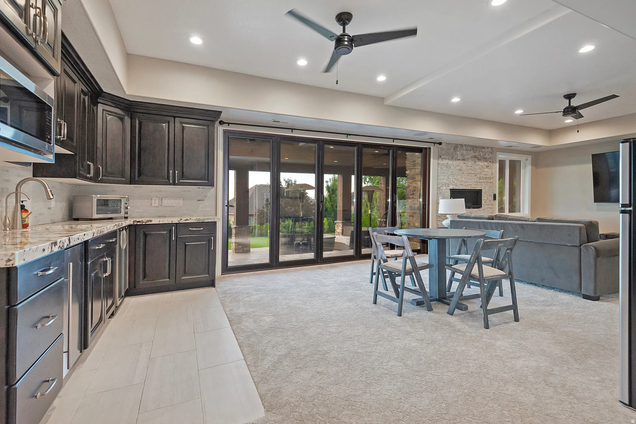 Kitchen featuring ceiling fan, light stone counters, stainless steel microwave, open floor plan, and healthy amount of natural light