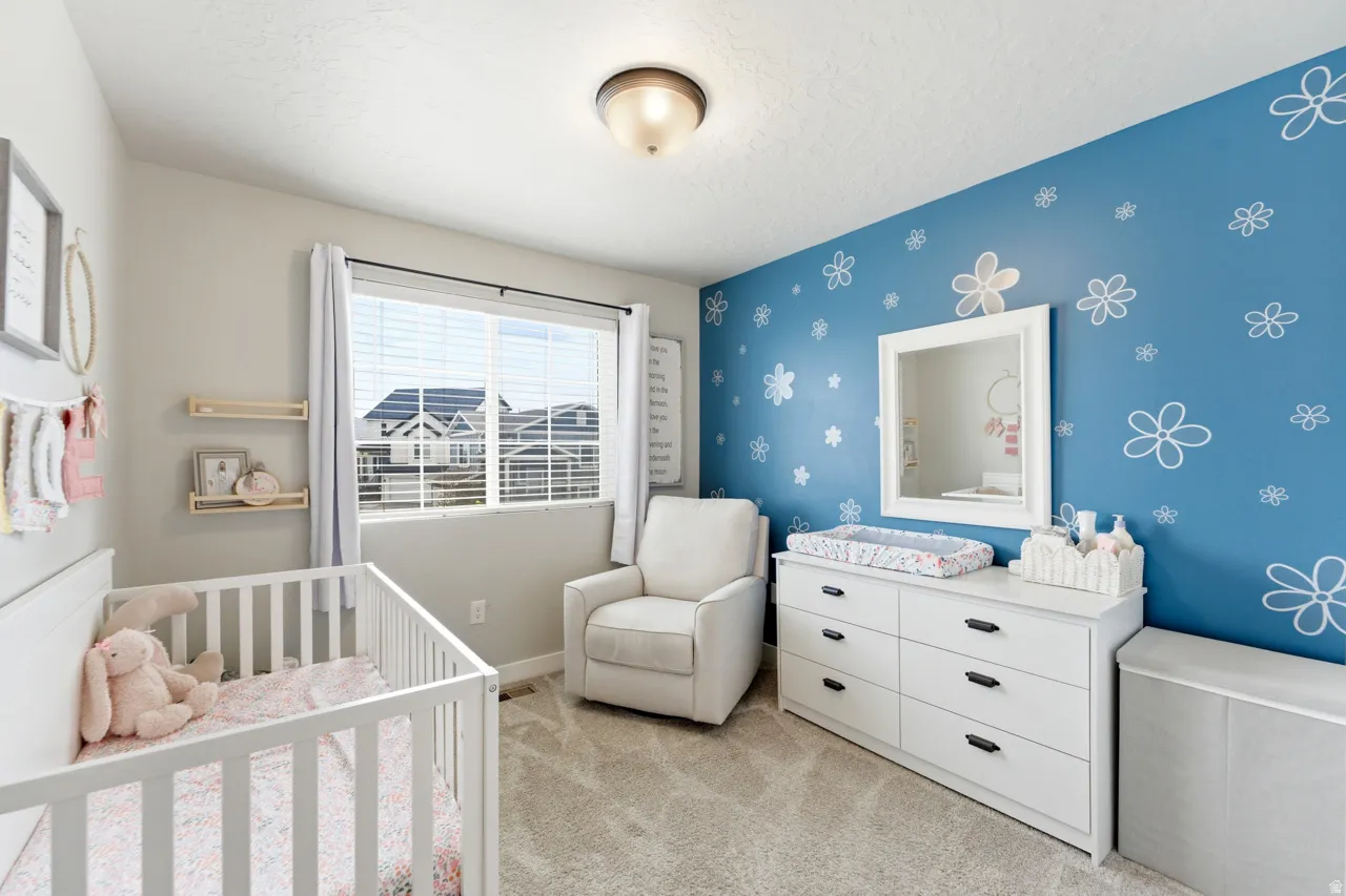 Bedroom featuring light carpet, a nursery area, an accent wall, wallpapered walls, and a textured ceiling