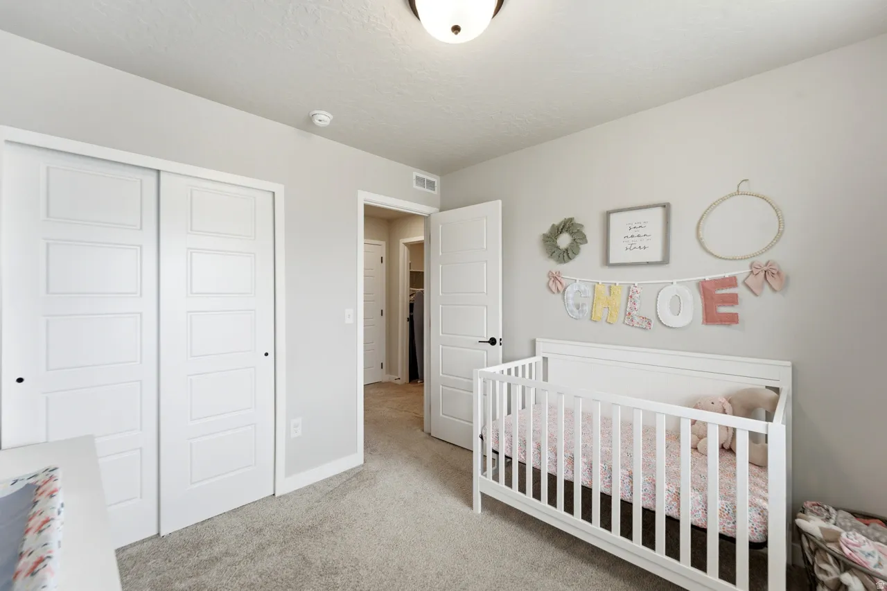 Bedroom featuring a closet, a crib, light colored carpet, and a textured ceiling