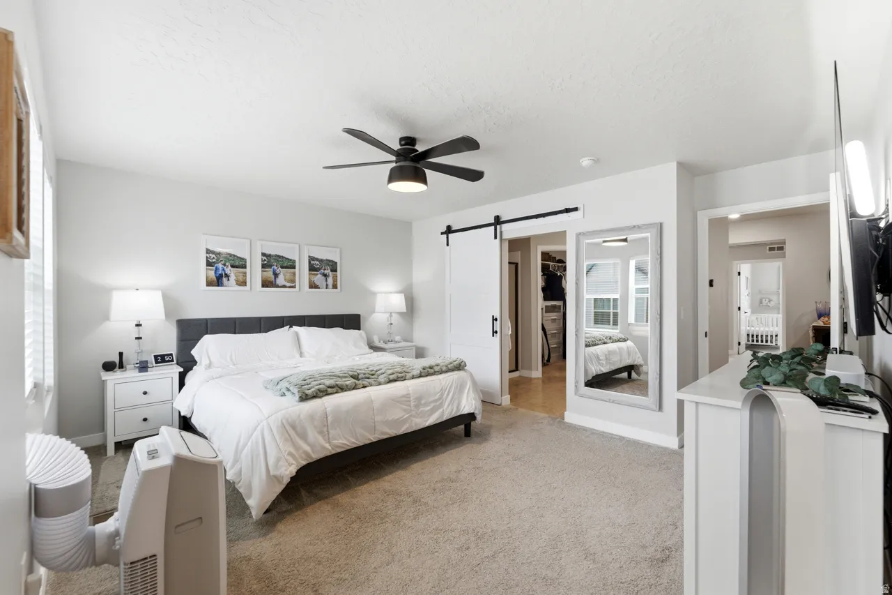 Bedroom with a barn door, light colored carpet, ceiling fan, and a textured ceiling