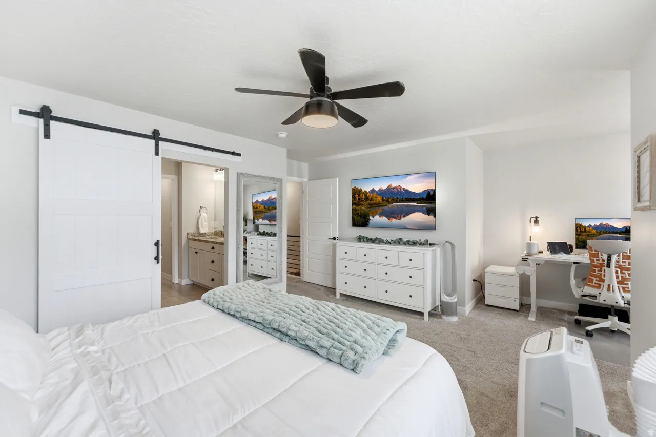 Bedroom with a barn door, ceiling fan, light carpet, ensuite bathroom, and an office area