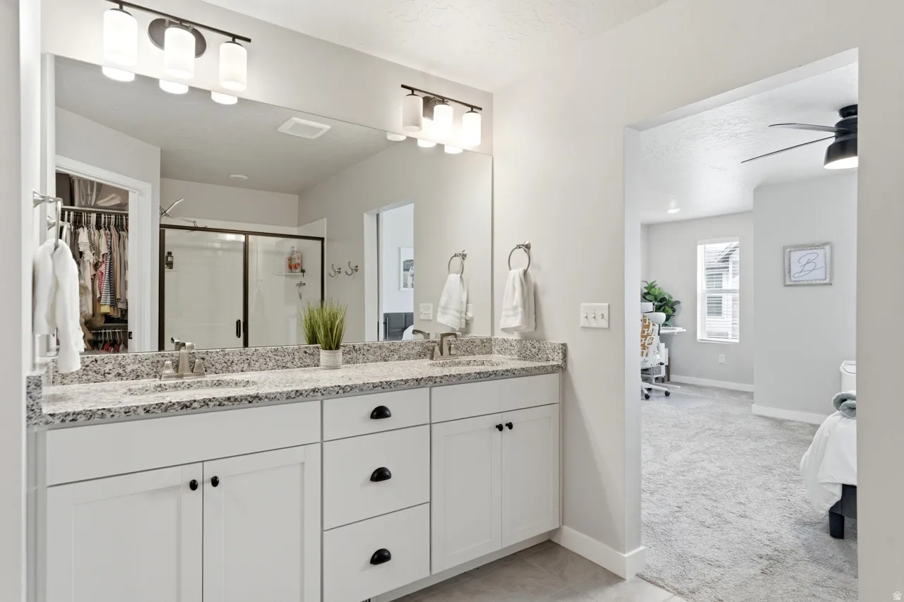 Full bath featuring light colored carpet, double vanity, a shower stall, a walk in closet, and a ceiling fan