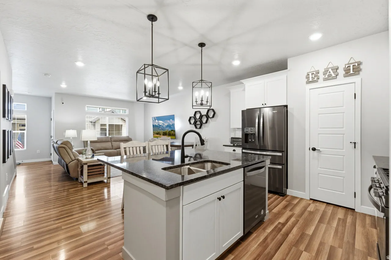 Kitchen with white cabinetry, dark stone counters, a center island with sink, open floor plan, and stainless steel appliances