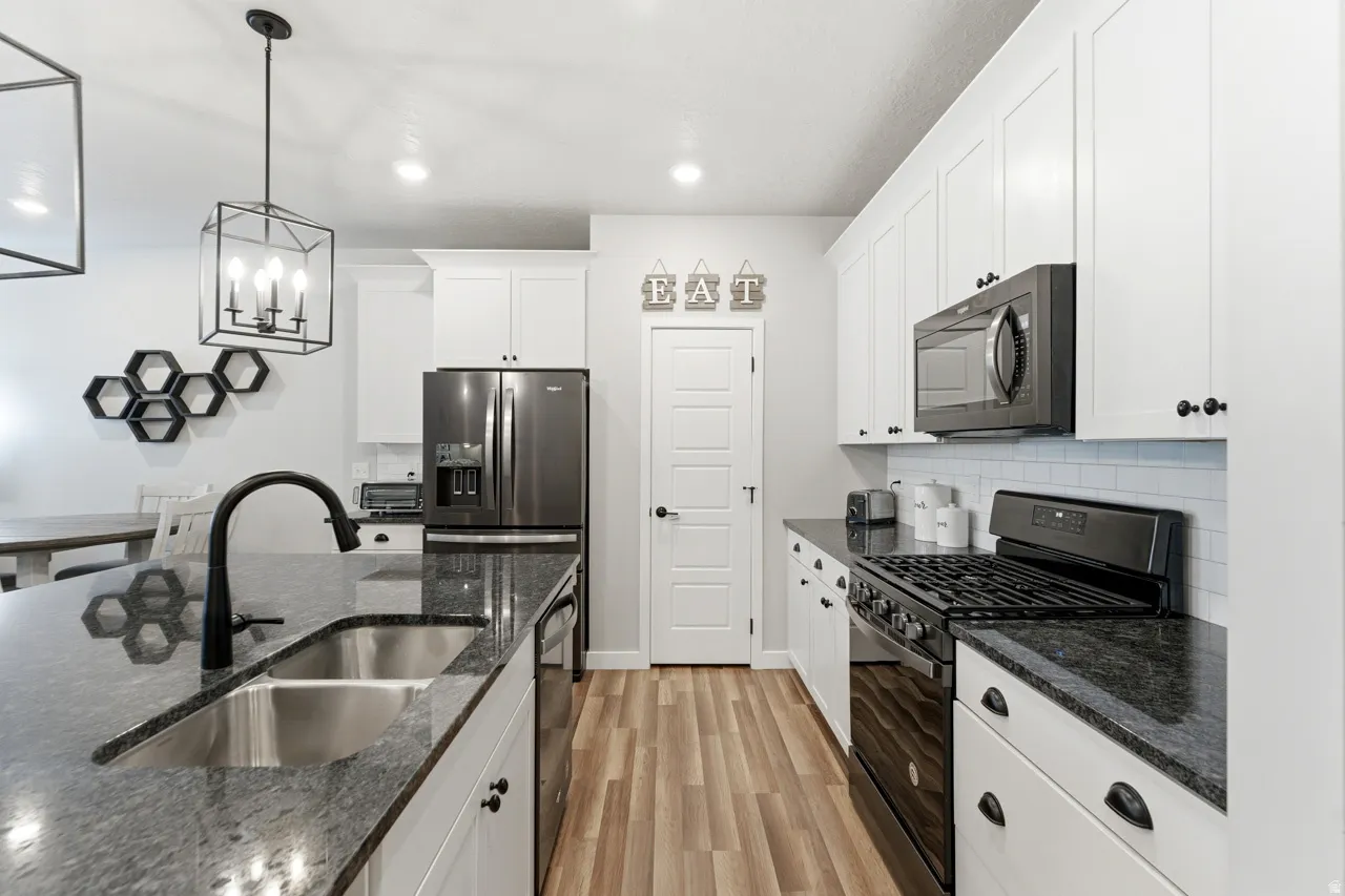 Kitchen with stainless steel appliances, white cabinetry, light wood-type flooring, and dark stone counters