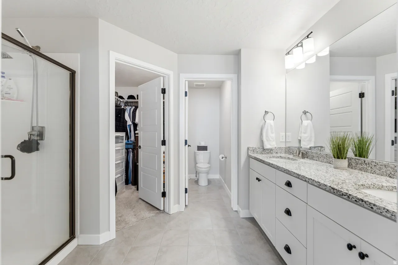 Full bathroom featuring double vanity, a stall shower, a walk in closet, a textured ceiling, and light tile patterned flooring