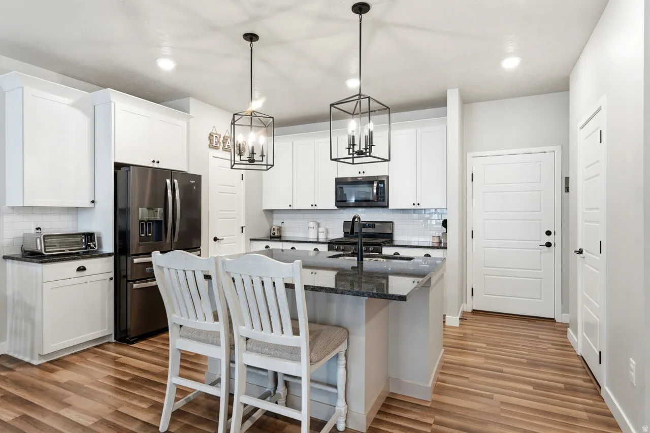 Kitchen featuring stainless steel appliances, a kitchen island with sink, white cabinets, and light wood-style floors