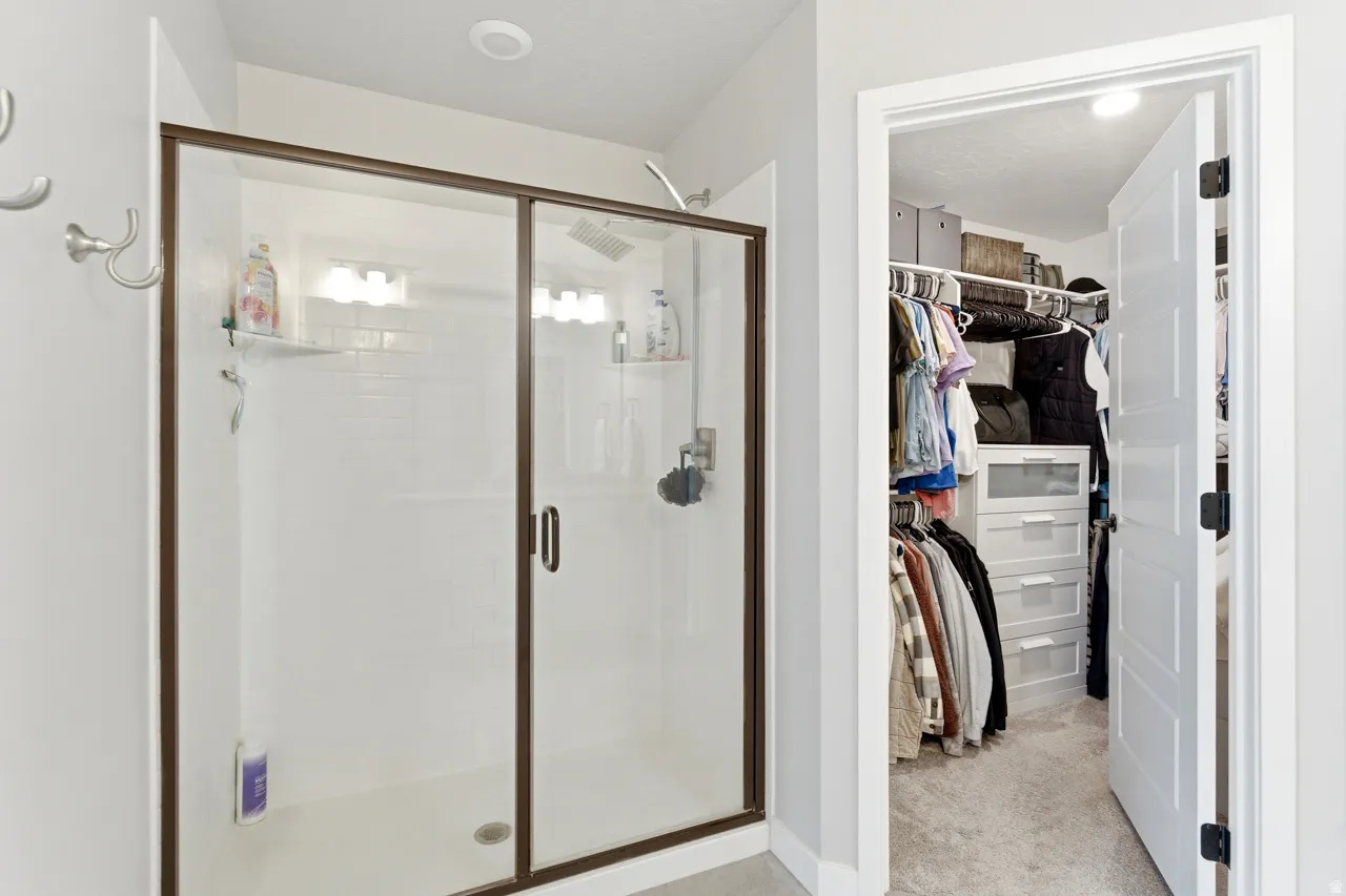 Full bath featuring a spacious closet, a shower stall, and light colored carpet