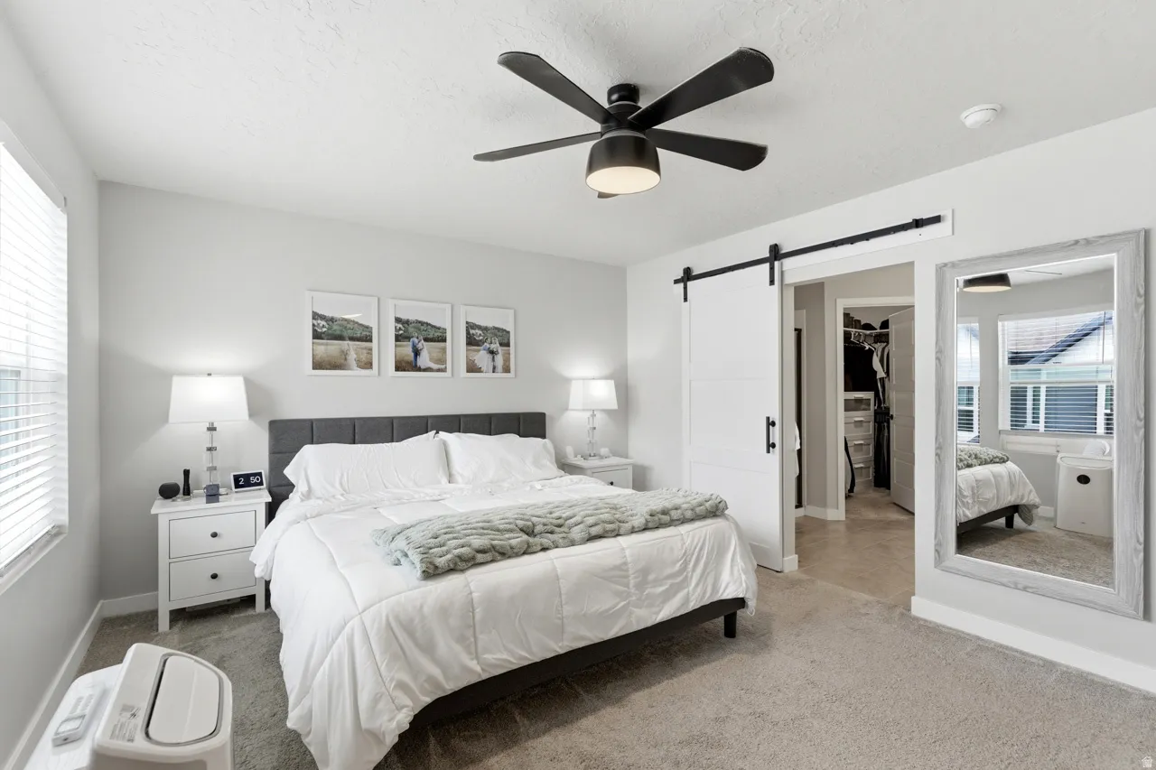 Carpeted bedroom featuring a barn door, a spacious closet, and a ceiling fan
