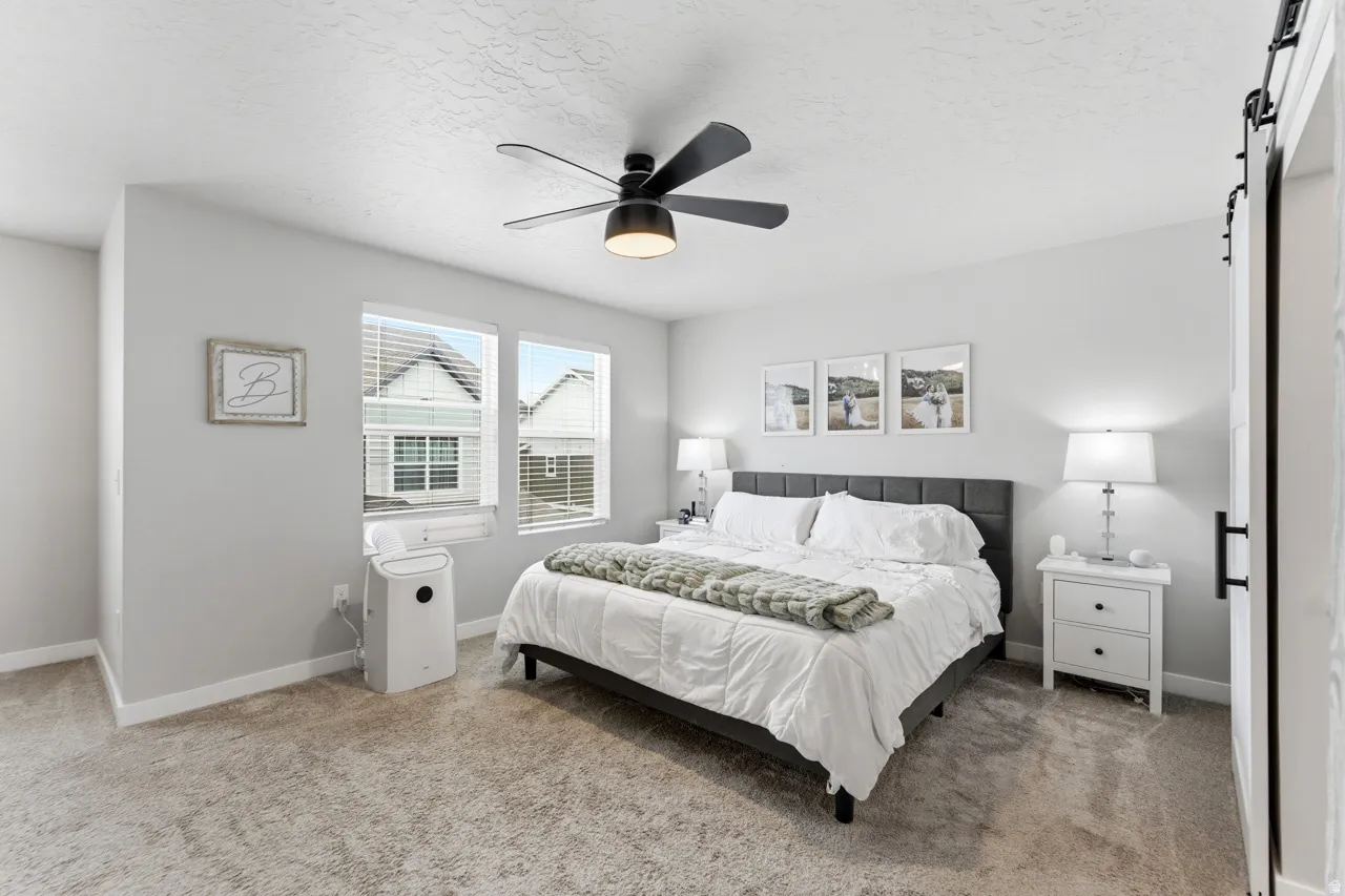 Bedroom with a barn door, a ceiling fan, light colored carpet, and a textured ceiling