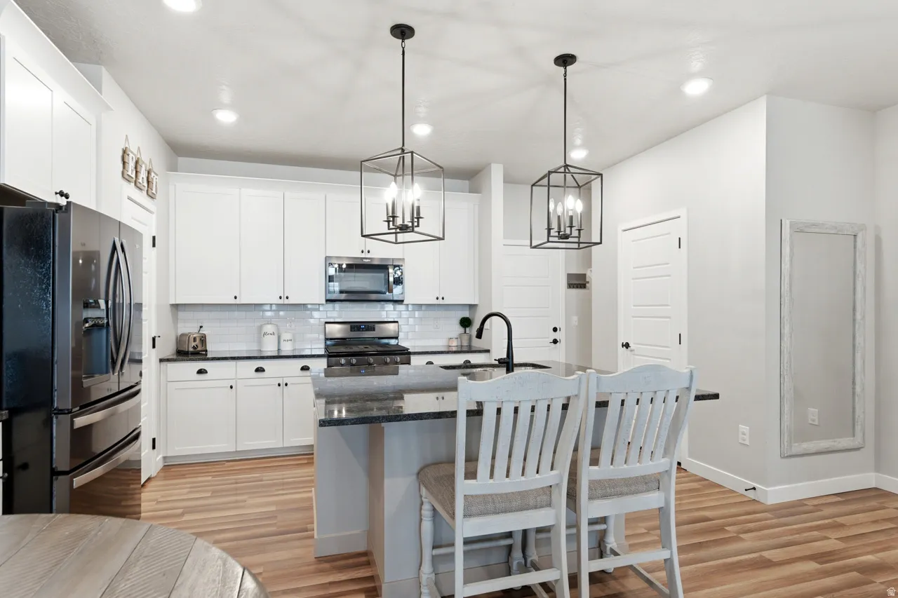 Kitchen with stainless steel appliances, a kitchen bar, a kitchen island with sink, and white cabinetry