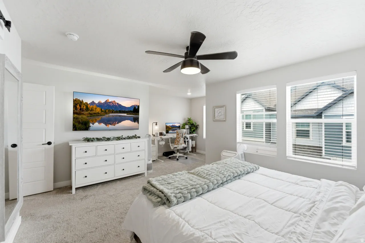 Carpeted bedroom with a ceiling fan and a desk