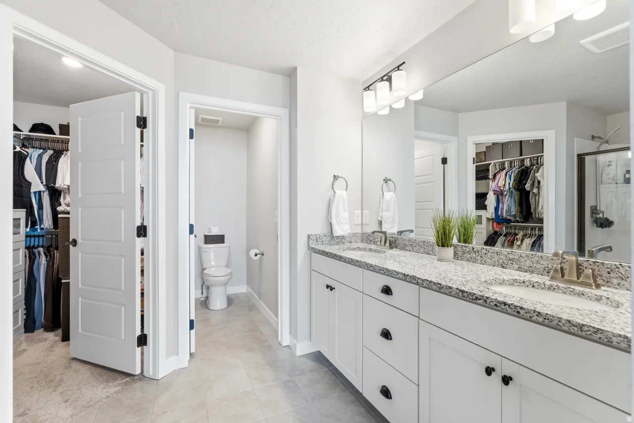 Full bathroom with a walk in closet, double vanity, a stall shower, and light tile patterned floors