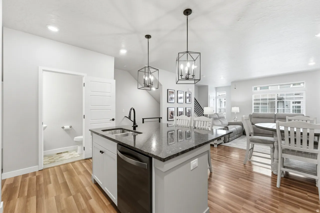 Kitchen with dishwasher, dark stone counters, a kitchen island with sink, a chandelier, and white cabinetry
