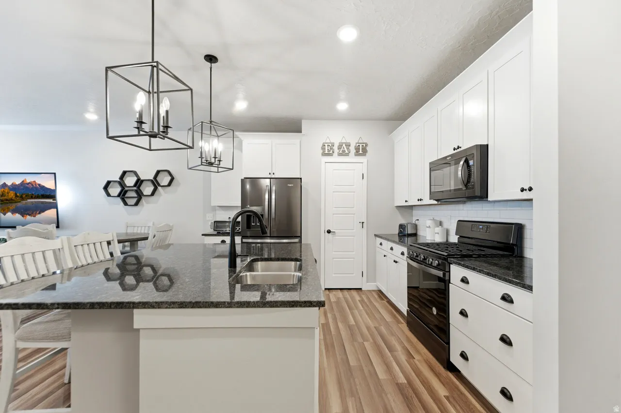 Kitchen with black gas range, a kitchen island with sink, light wood-style flooring, and dark stone counters